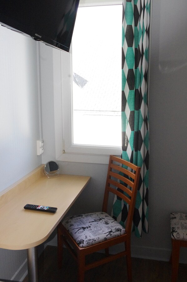 A small room with a window, a wooden chair with a patterned cushion, a small table, and a remote control on the table.