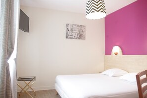 A bedroom with a bed, a wall-mounted TV, a small folding chair, a wall clock, and a bedside lamp. - Hôtel de Paris (Barneville-Carteret)