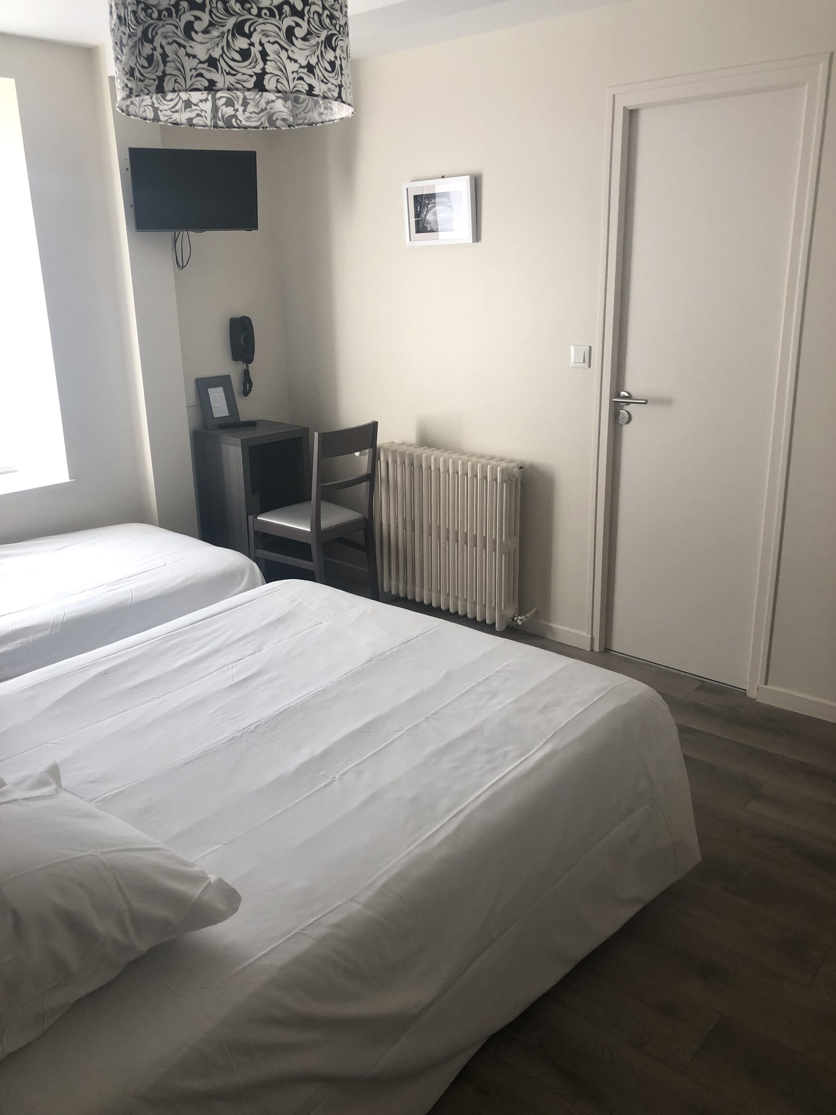 A bedroom with two beds, a radiator, a desk with a chair, a framed picture, and a door.