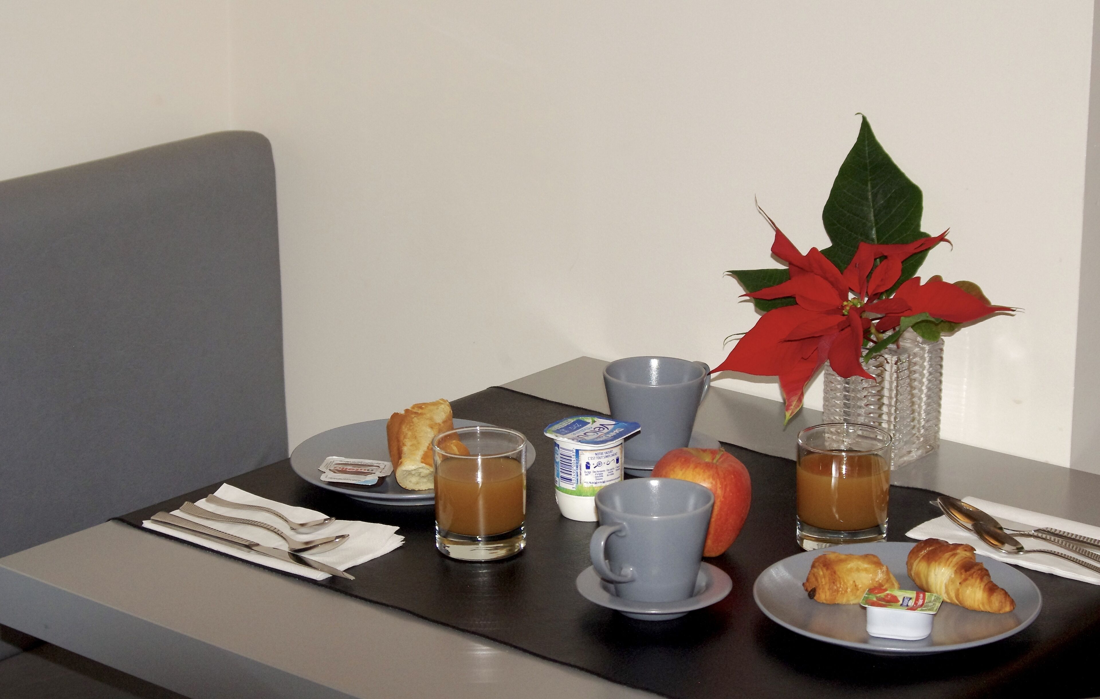 Mesa com pães de chocolate, uma fruta, uma bebida e uma planta em vaso.