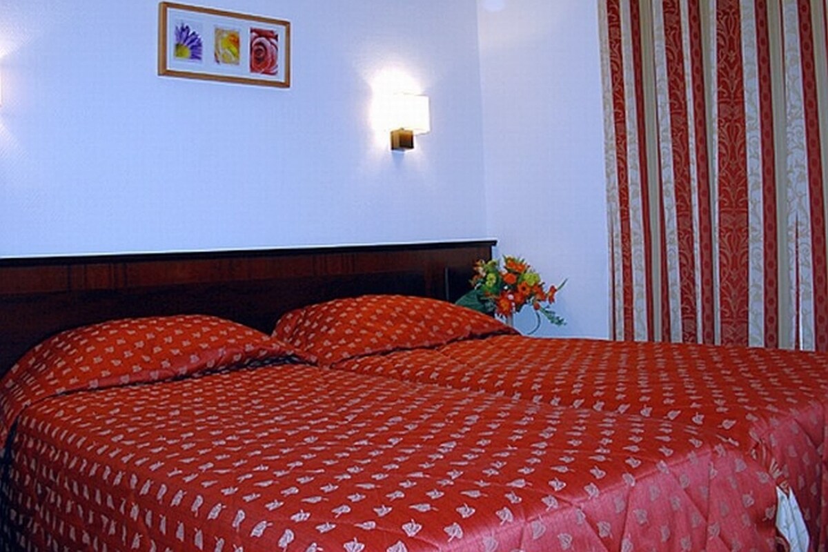 Een hotelkamer met een groot bed, een nachtkastje met een bloevas en een wandlamp.