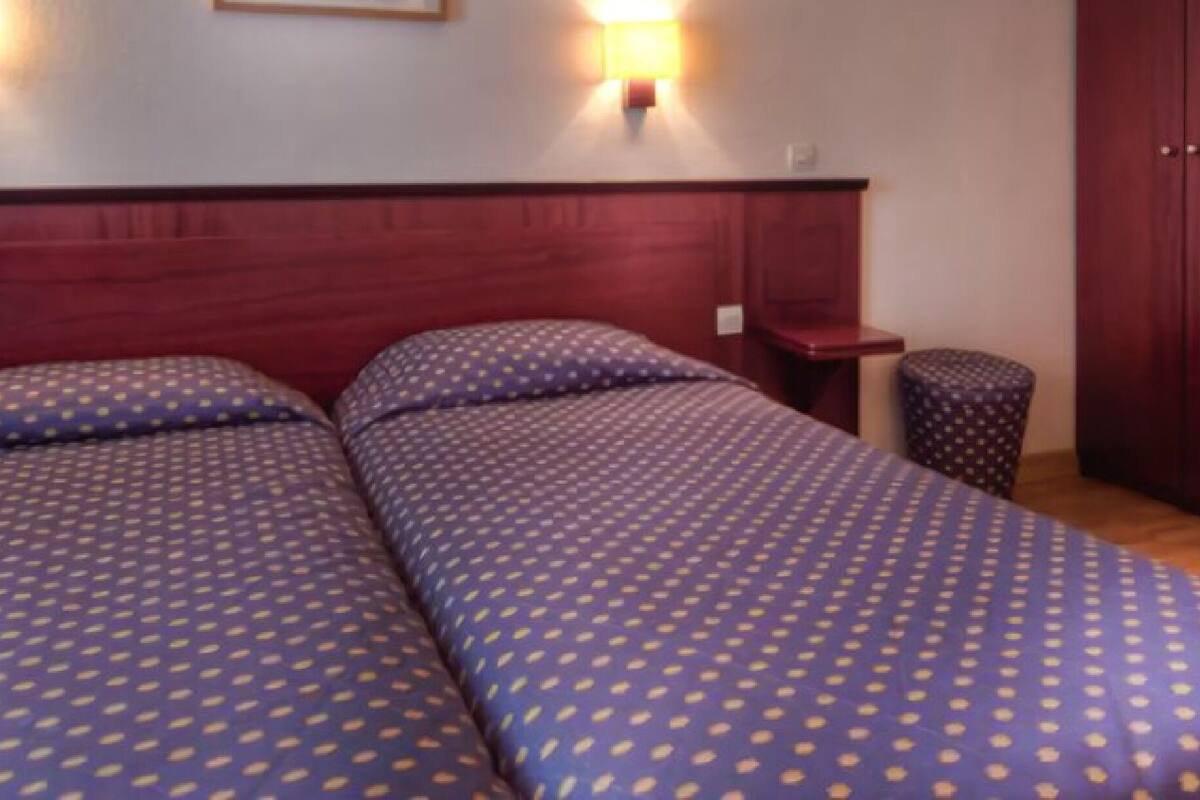 A hotel room with two beds, wooden headboard, bedside tables, and a wardrobe.
