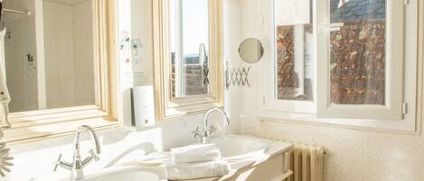A bathroom with two sinks, a mirror, a window, and a radiator.