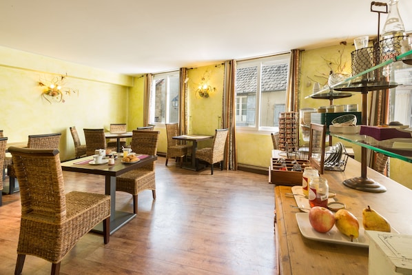 A dining area with wicker chairs, a wooden table, and a buffet setup with food items.