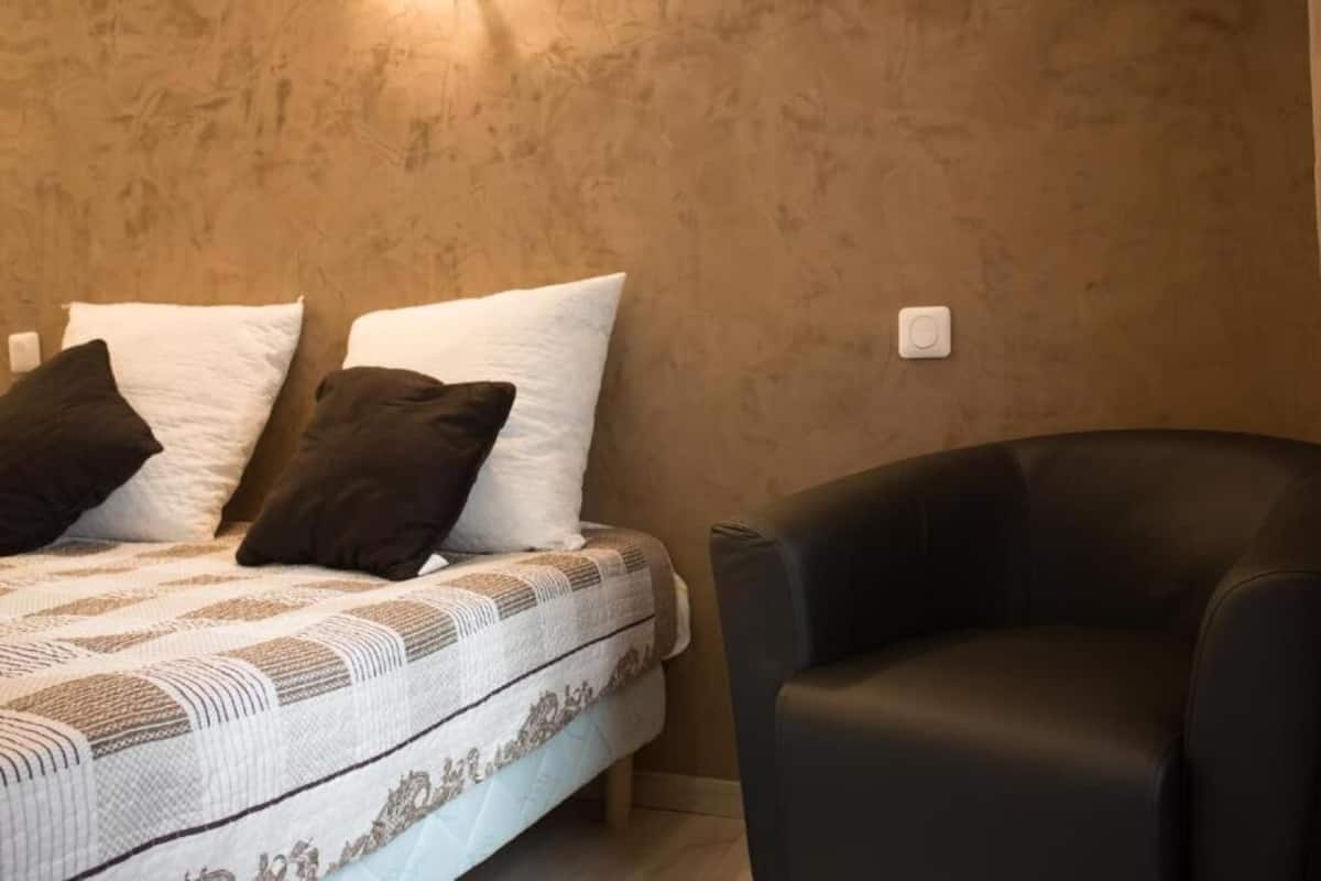 Ein Schlafzimmer mit einem Bett, zwei Kissen, einem schwarzen Stuhl und einer strukturierten Wand.
