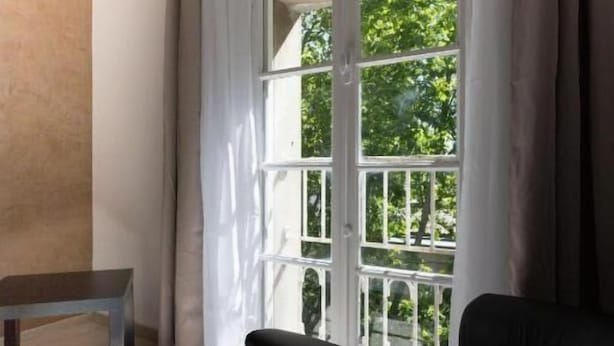 Een kamer met een groot raam, een bed, een stoel en een klein tafeltje.