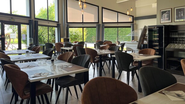 Un restaurante con varias mesas y sillas, ventanas amplias y lámparas colgantes.