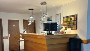Zona de recepción de un hotel con un mostrador de madera, una computadora y un perchero para llaves en la pared.