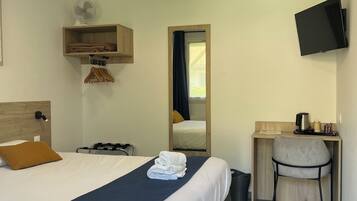 Una habitación de hotel con cama, escritorio, silla, televisor, ventilador y ventana.