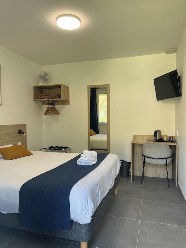 A hotel room with a bed, a desk, a chair, a TV, a fan, and a window.