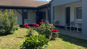Un edificio con techo de tejas, un patio cubierto y un jardín con flores rojas.