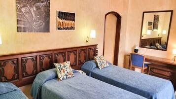 A hotel room with two single beds, a desk with a chair, a mirror, and a wall-mounted artwork.