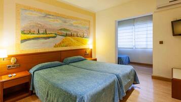 Una habitación de hotel con dos camas, un cuadro en la pared, un televisor y una ventana con persianas.