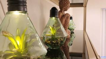 A Buddha statue in a hallway with decorative light fixtures containing plants.