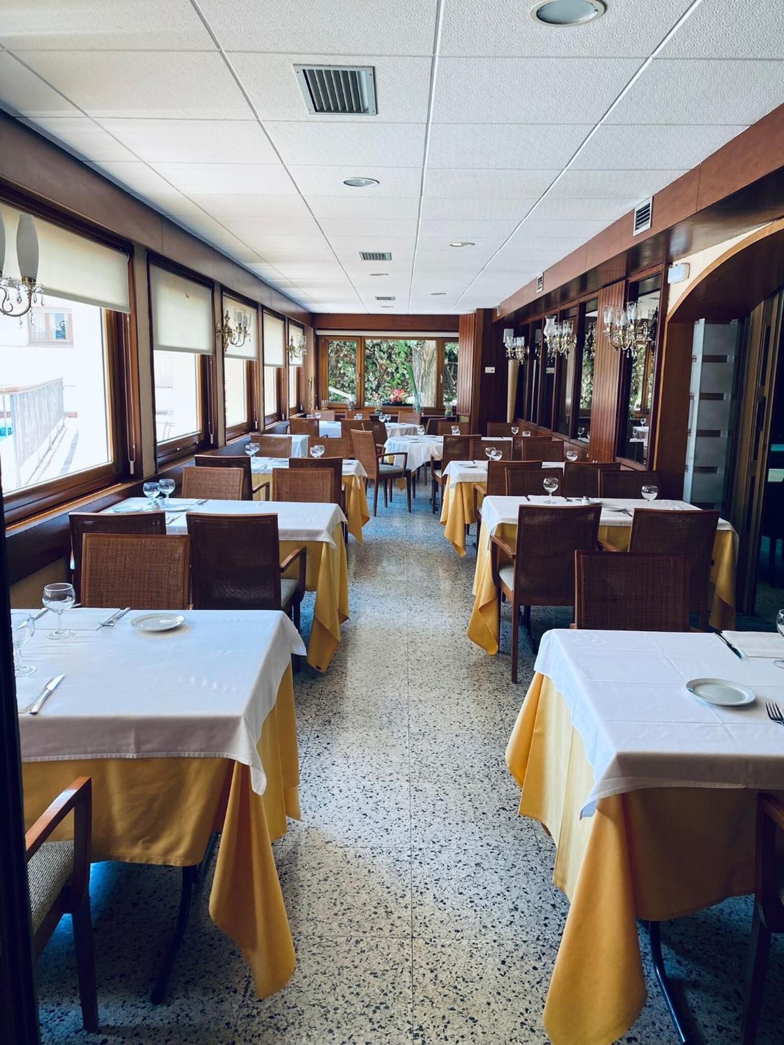 A restaurant with multiple tables, each set with white tablecloths and yellow chair covers.