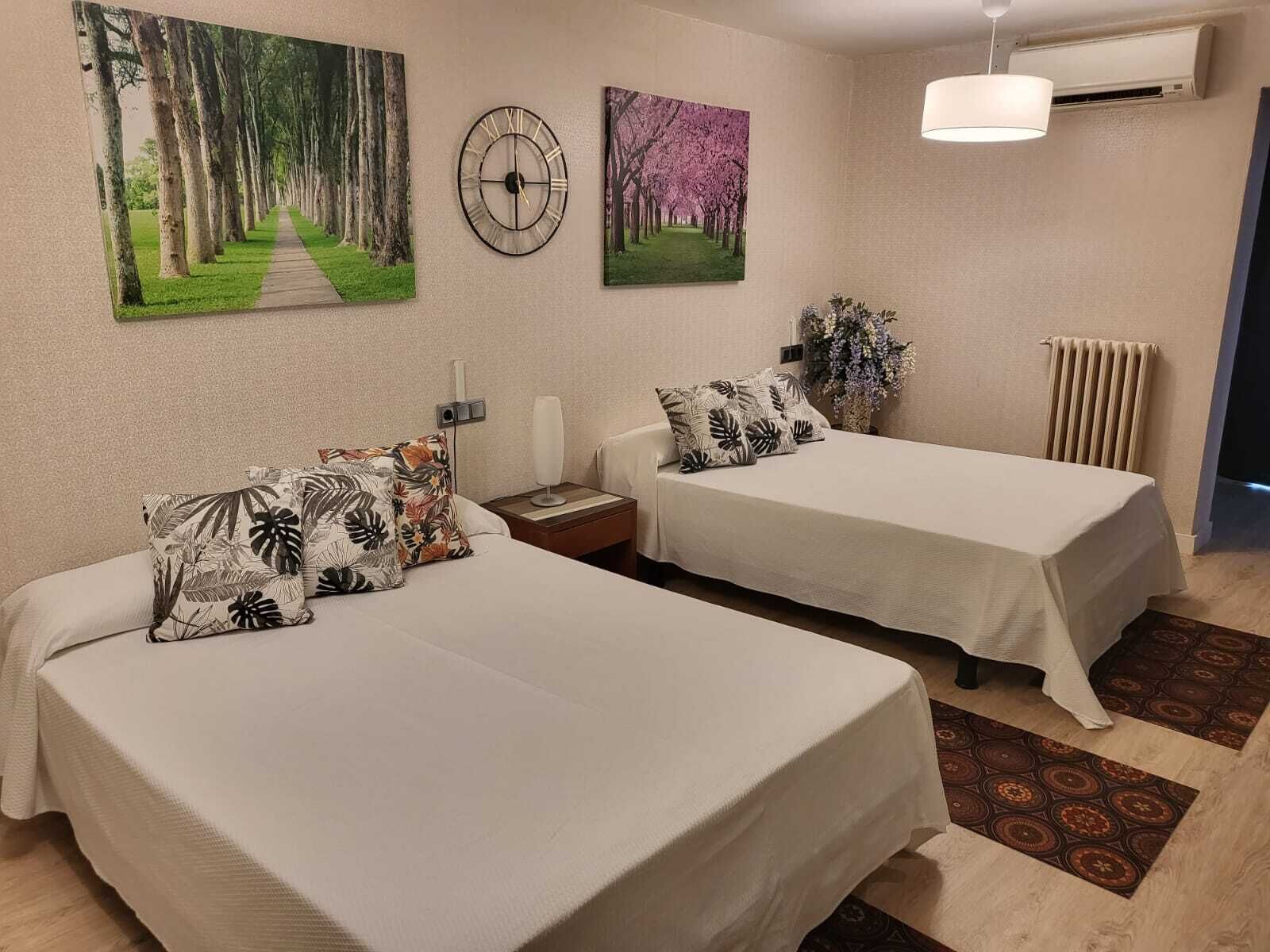A hotel room with two beds, a clock, and two paintings on the wall.