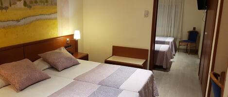 Habitación de hotel con dos camas, una mesita de noche con lámpara, un cuadro en la pared y un televisor en la esquina.