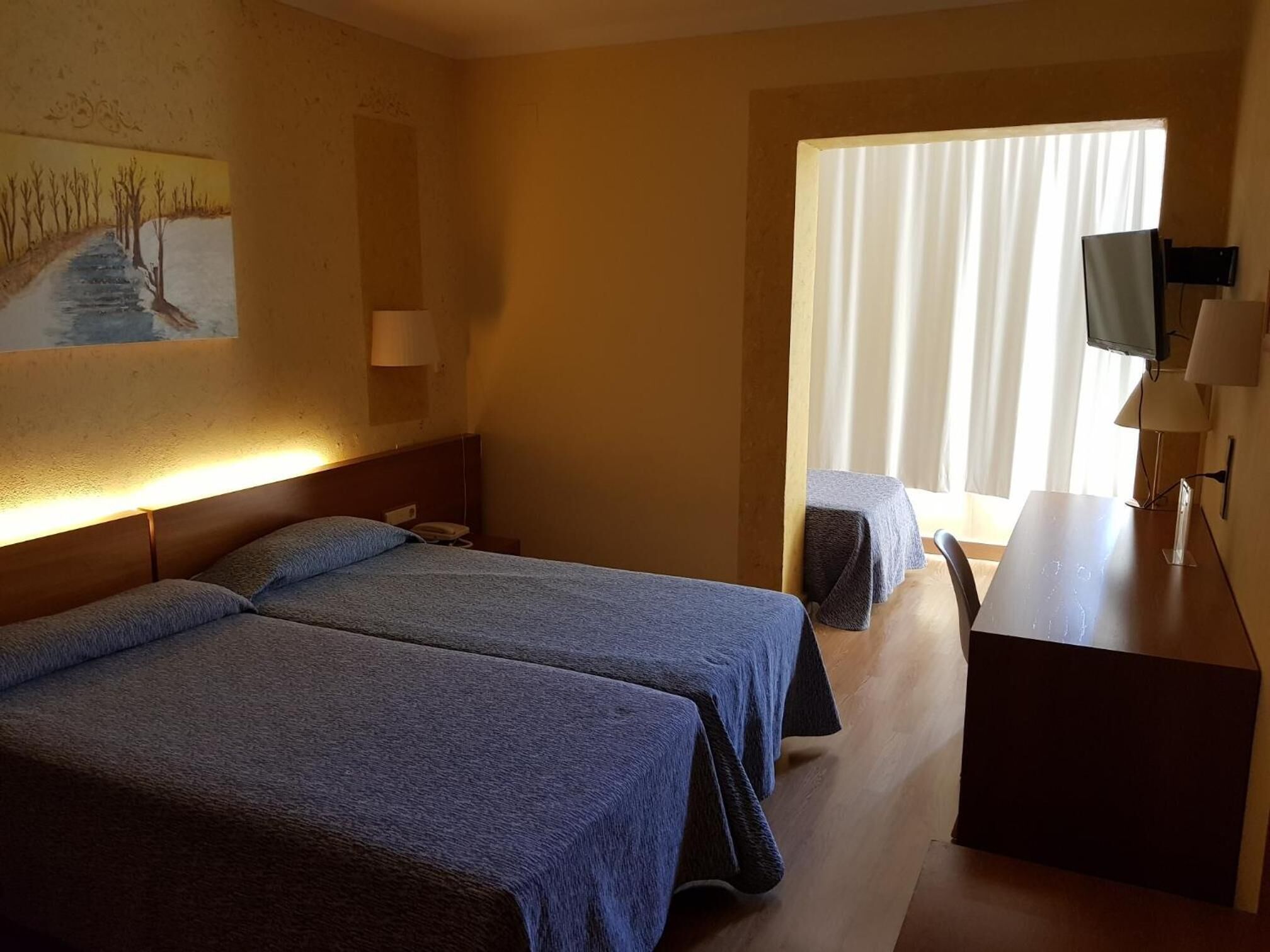 A hotel room with two beds, a desk, a TV, and a window with curtains.
