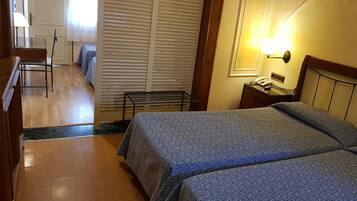 A hotel room with two beds, a desk, a chair, a lamp, and a window with blinds.