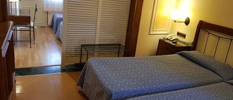 Una habitación de hotel con dos camas, un escritorio, una silla, una lámpara y una ventana con persianas.