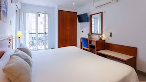 Quarto de hotel com uma cama grande, uma escrivaninha com cadeira, uma televisão fixada na parede e uma varanda com mobiliário de exterior.