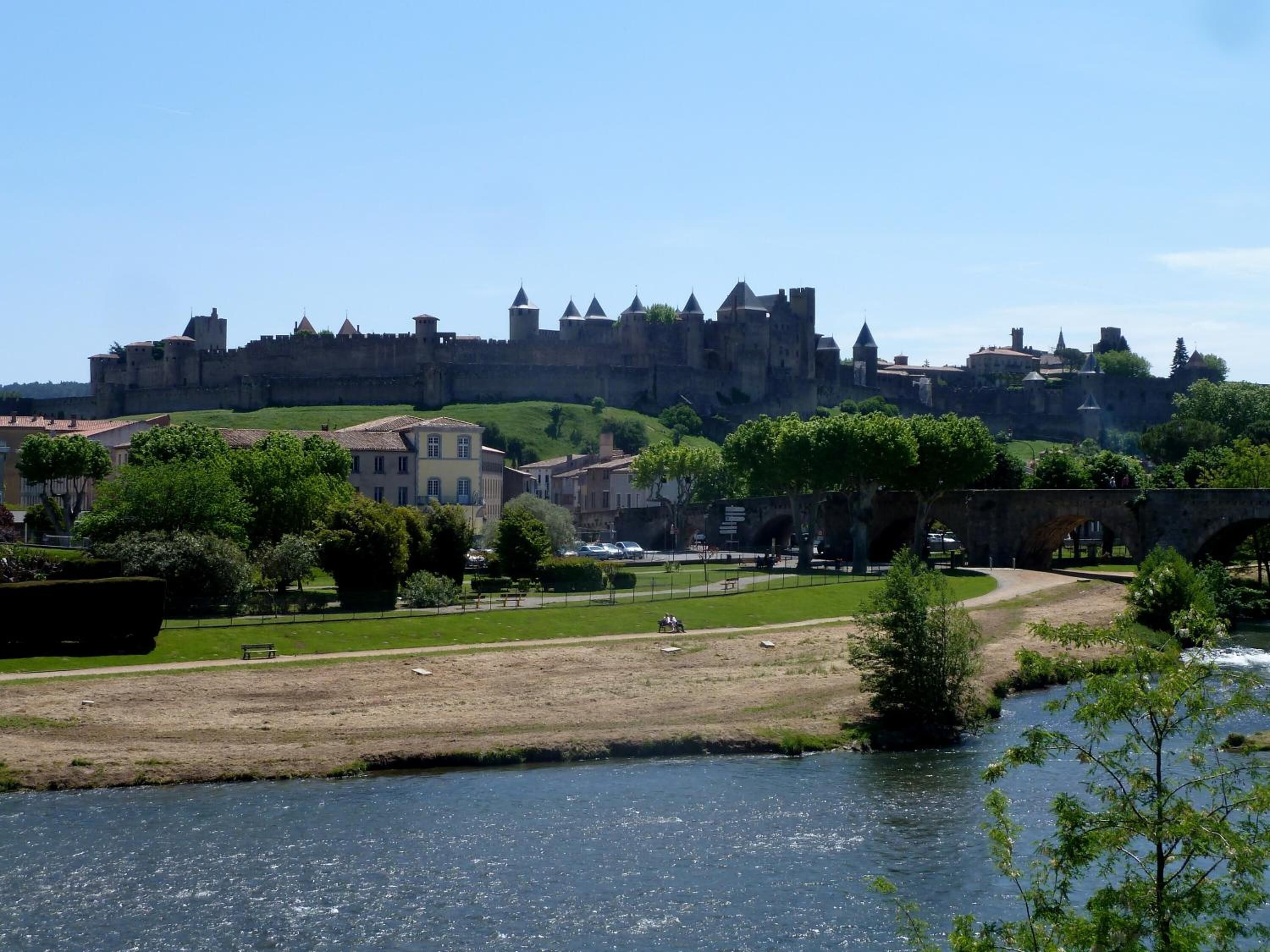 Vista de um castelo histórico numa colina, um rio em primeiro plano e uma ponte a ligar o castelo à cidade abaixo.