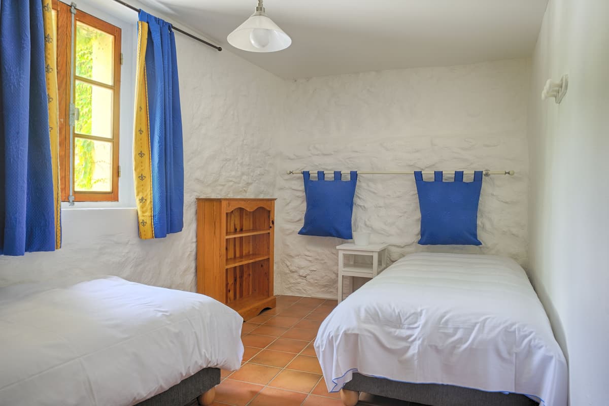 A bedroom with two beds, a wooden wardrobe, a small table, and a window with curtains.