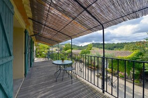A wooden deck with a table and chairs, a metal railing, and a view of a green landscape. - Domaine de Fraisse (Leuc)