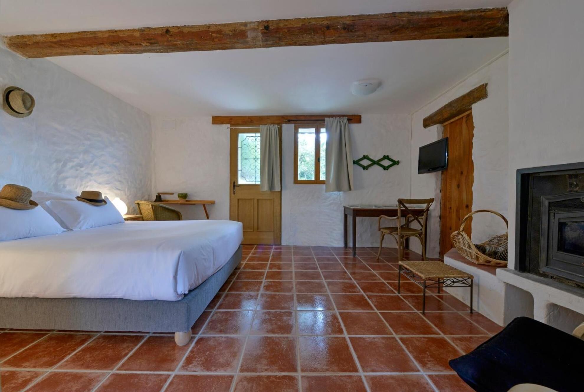 A room with a bed, a small table, a chair, a television, and a fireplace.