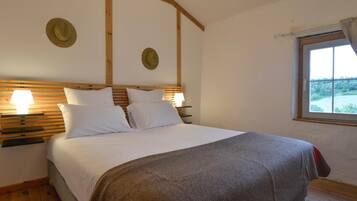 Un dormitorio con cabecera de madera, dos mesitas de noche con lámparas, una cama grande con ropa blanca y una ventana con vistas a zonas verdes.