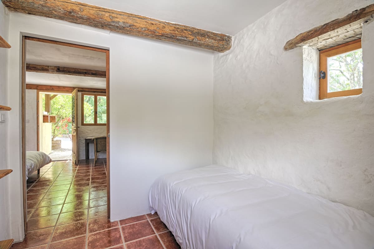 A bedroom with a bed, a small window, and a door leading to another room.