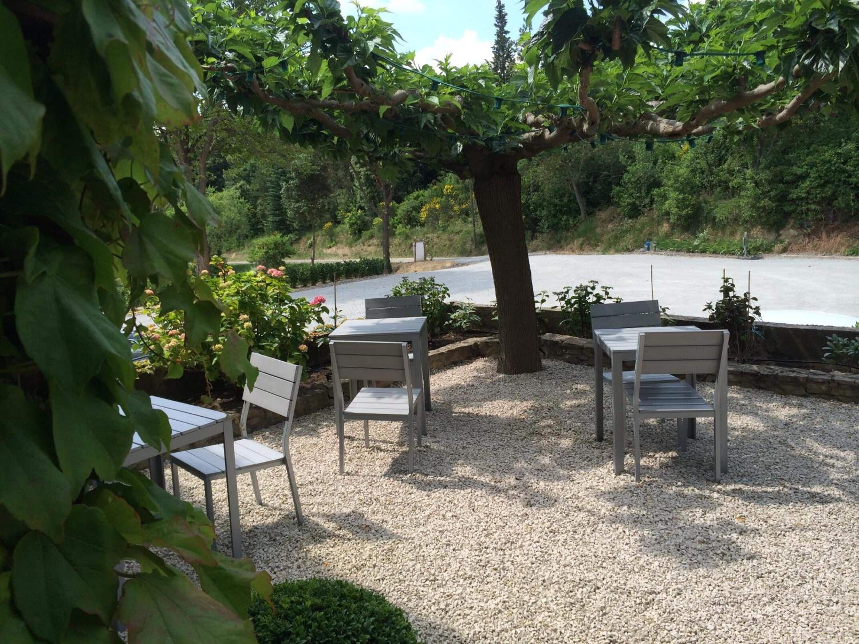 An outdoor seating area with four white chairs and a table, surrounded by gravel and greenery.