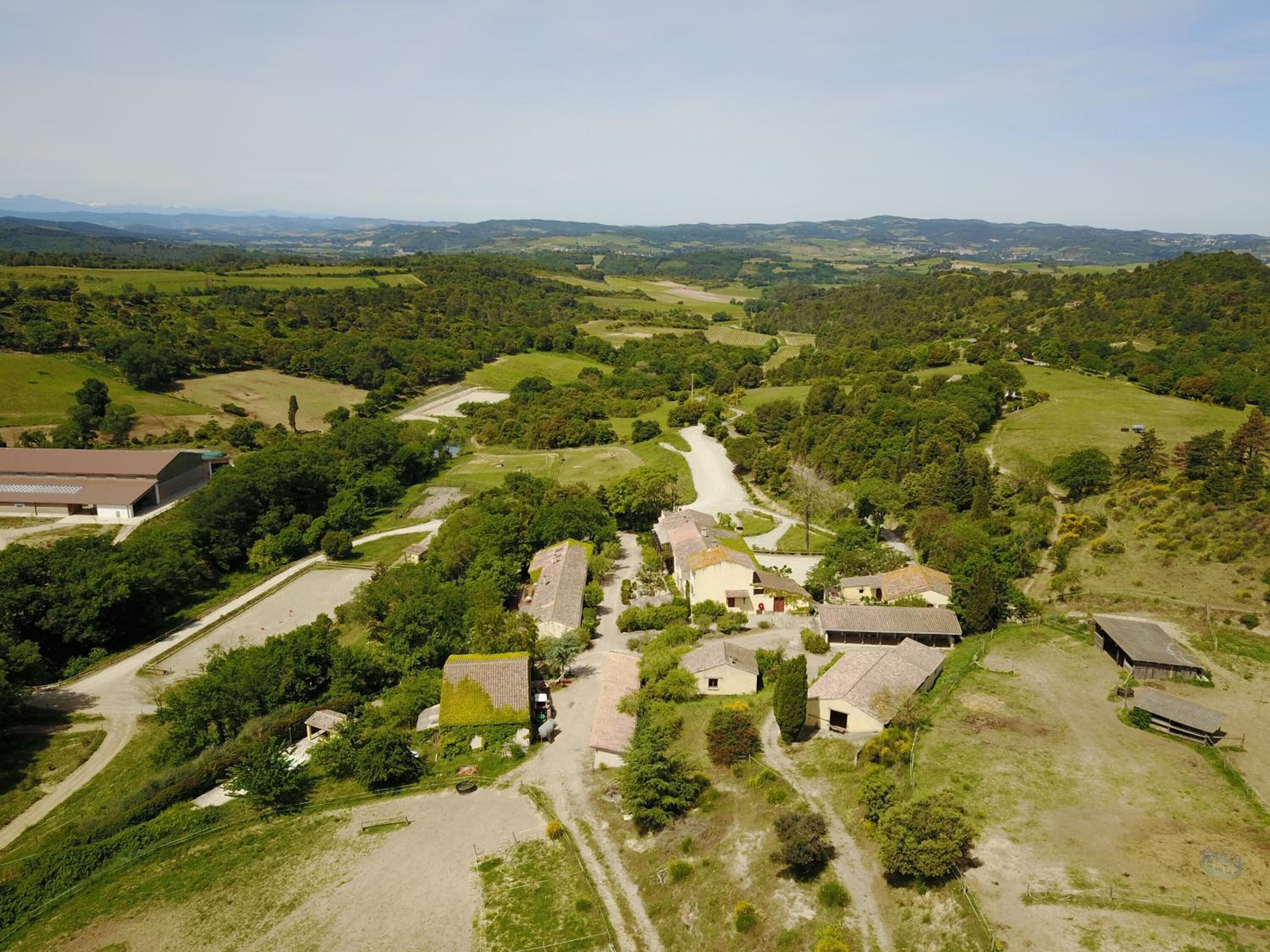 An aerial view of a rural area with scattered houses, a dirt road, and green fields.