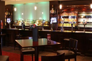 Uma área de bar com diversas opções de assento, variedade de garrafas de bebidas e uma tela de televisão.
