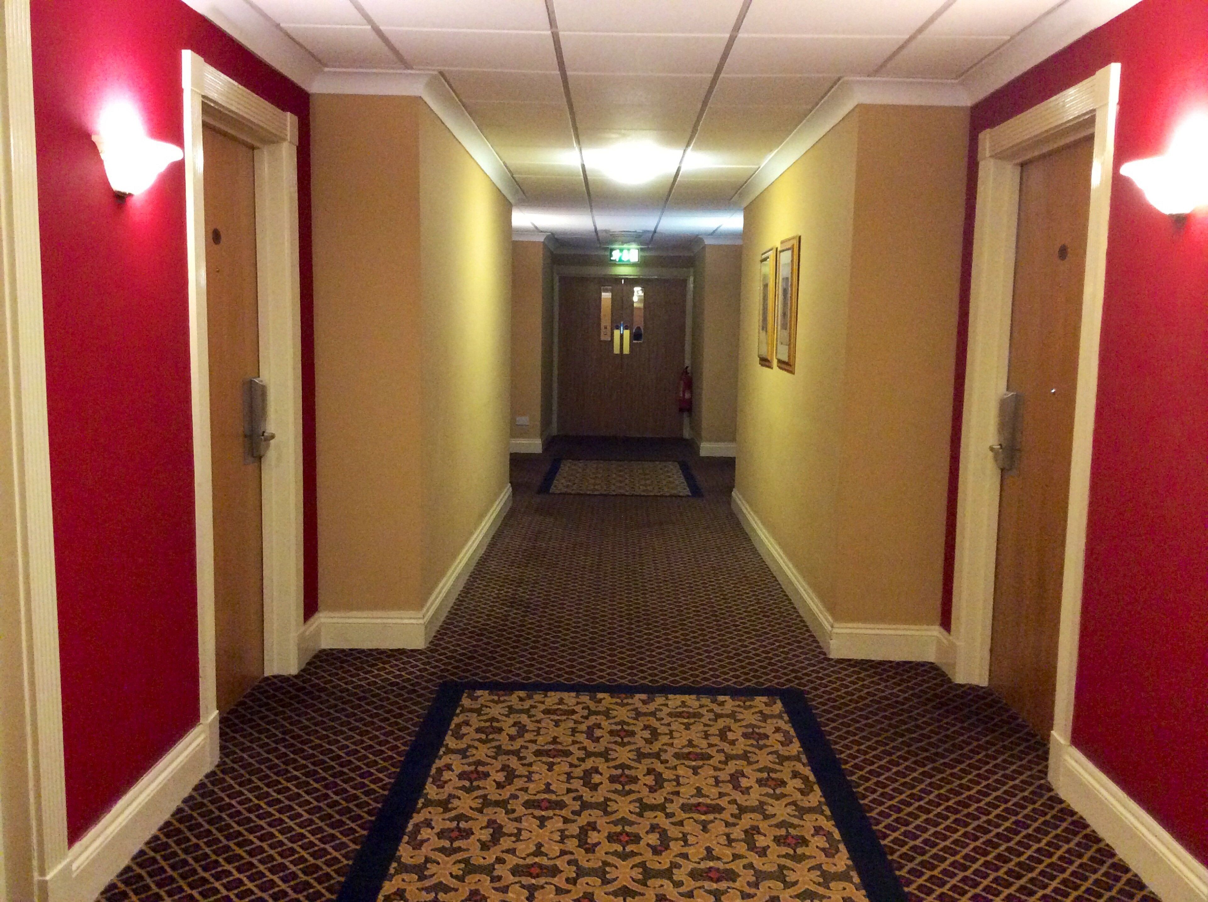 A hotel hallway with carpeted floors, red walls, and doors on both sides.