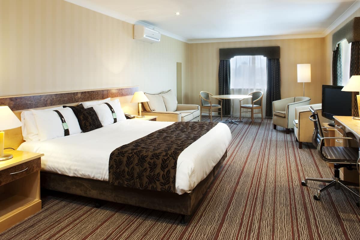 A hotel room with a large bed, a desk with a chair, a TV, and a small table with chairs.