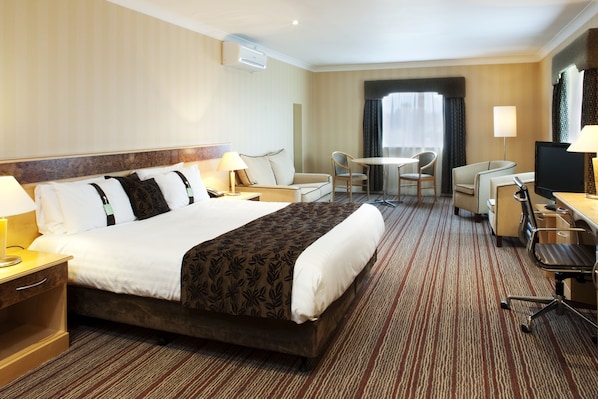 A hotel room with a large bed, a desk with a chair, a TV, and a small table with chairs.