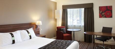 Habitación de hotel con una cama grande, un escritorio, una silla, una mesita y una ventana con cortinas.