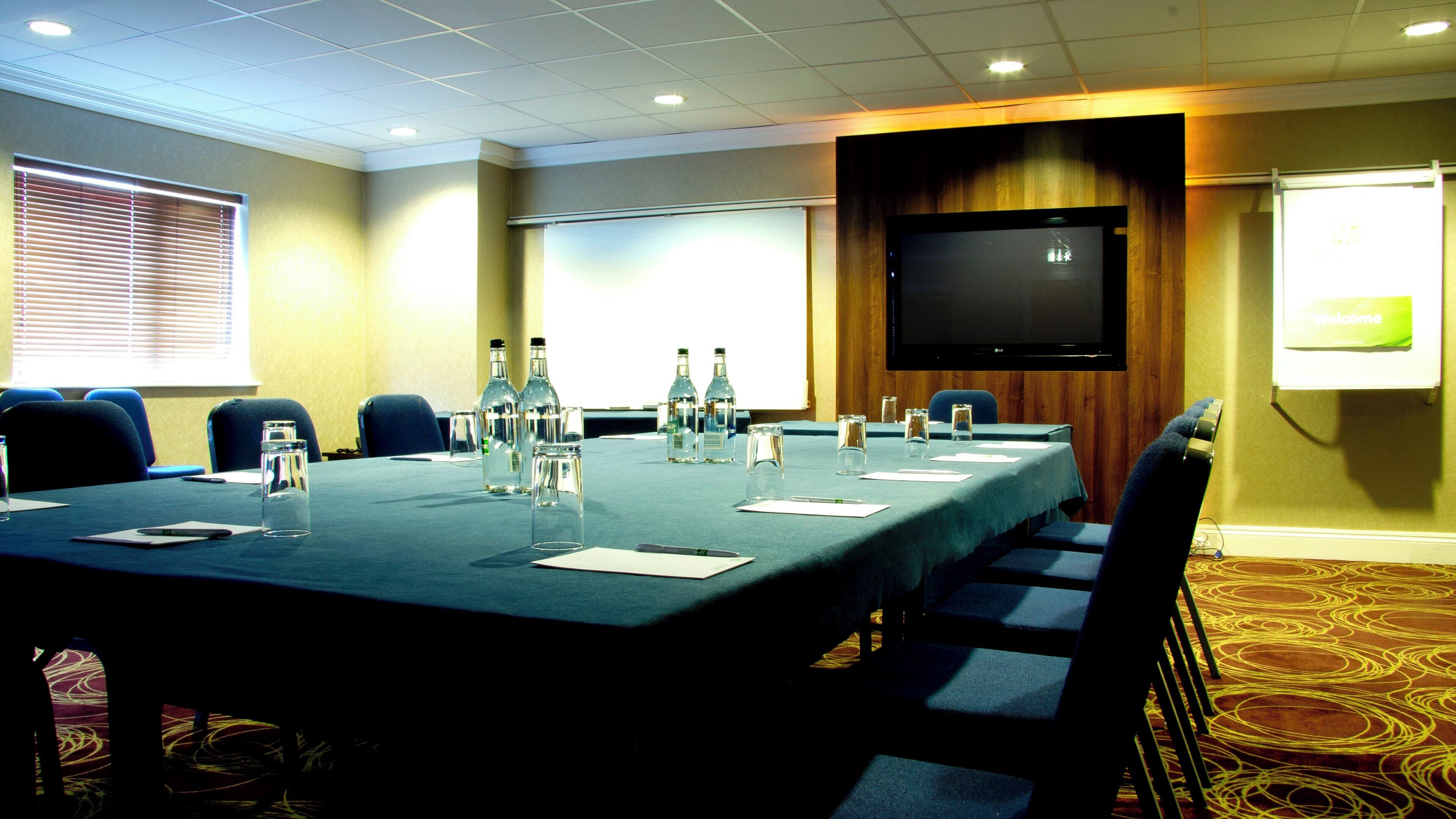 A conference room with a long table, chairs, water bottles, glasses, a projector screen, and a television.