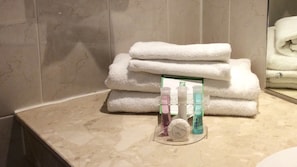 A bathroom with a stack of white towels, a glass display case with toiletries, and a mirror reflecting the towels.