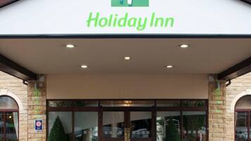 The exterior of a Holiday Inn hotel with a stone facade, large glass entrance, and a sign above the doors.