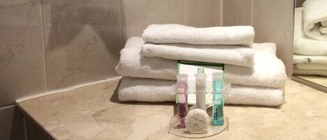 Un baño con una pila de toallas blancas, un espejo y un estante con artículos de tocador.