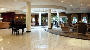 A spacious lobby with a grand piano, comfortable seating, and a reception area.