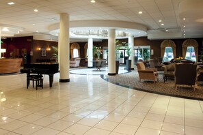 A spacious lobby with a grand piano, comfortable seating, and a reception area.