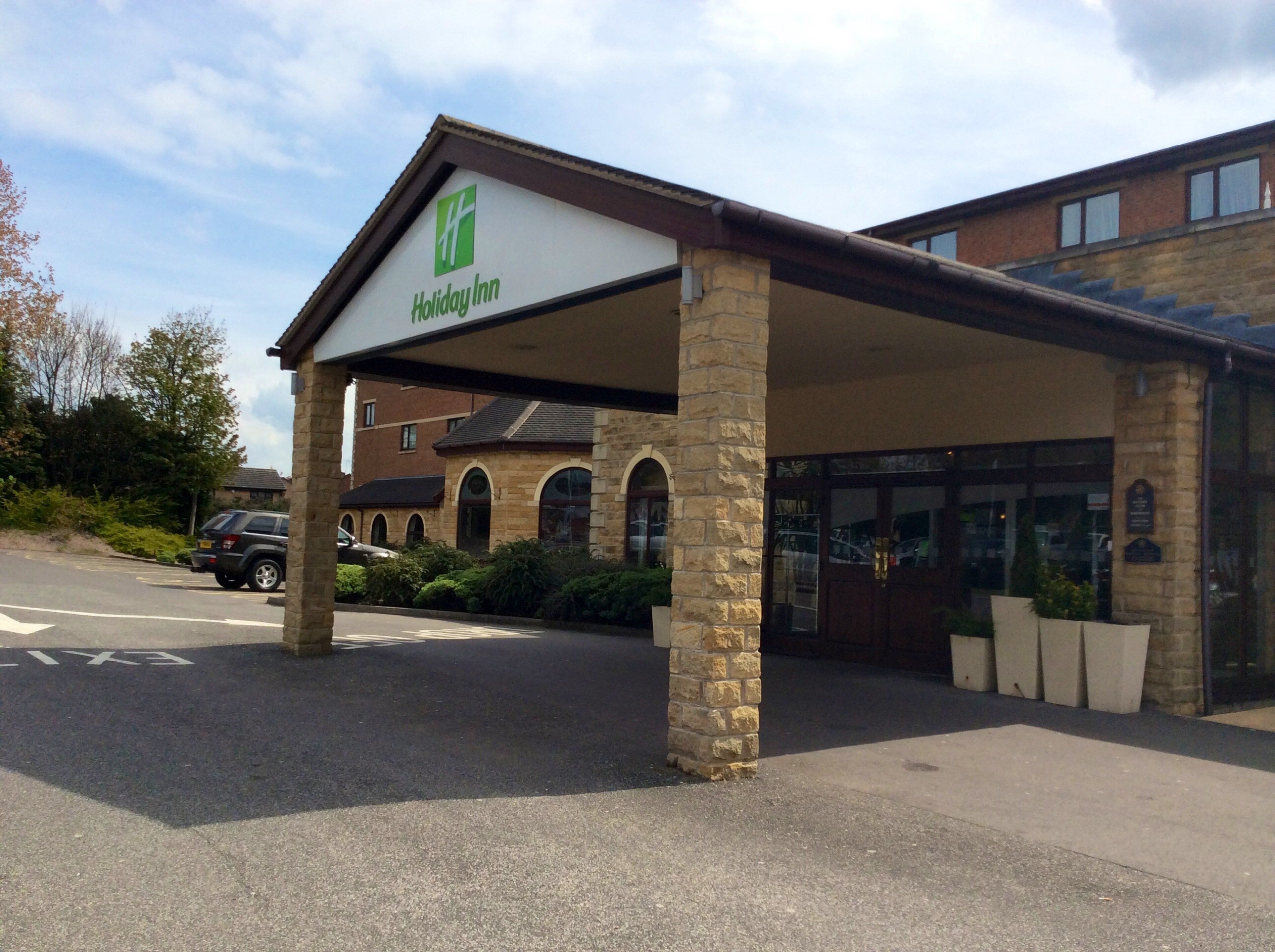 A Holiday Inn with a covered entrance, stone pillars, and a brick building in the background.