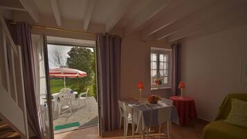 A room with a dining table, chairs, a green sofa, and a window with curtains.