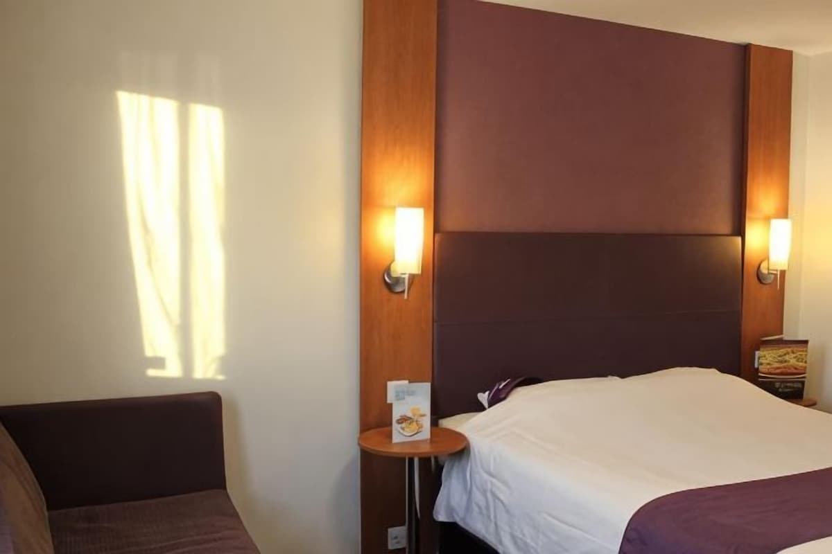 A hotel room with a bed, bedside tables, and wall-mounted lamps.