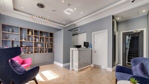A modern living room with a herringbone floor, a reception desk, and a kitchen area. - Mornington Hotel London Victoria (London)