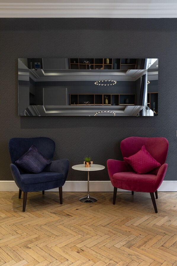 Una habitación con dos sillones, una pequeña mesa redonda y un espejo grande en la pared.