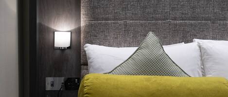 A hotel room with a large bed, a bedside table with a telephone, and a wall-mounted light.